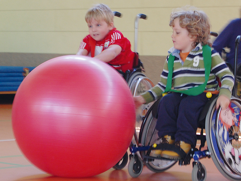 Zwei junge Rollstuhlfahrer beim Spiel mit dem Pezziball